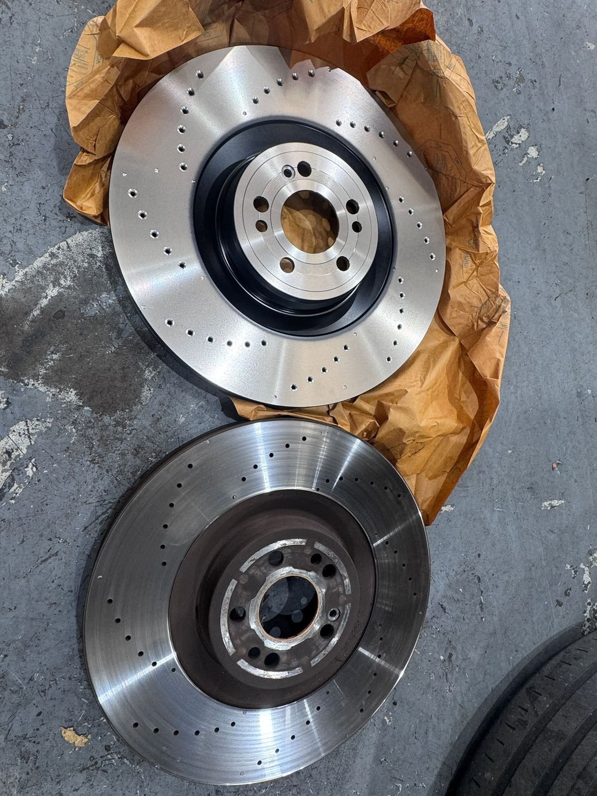 A new drilled brake rotor next to the worn one it replaced