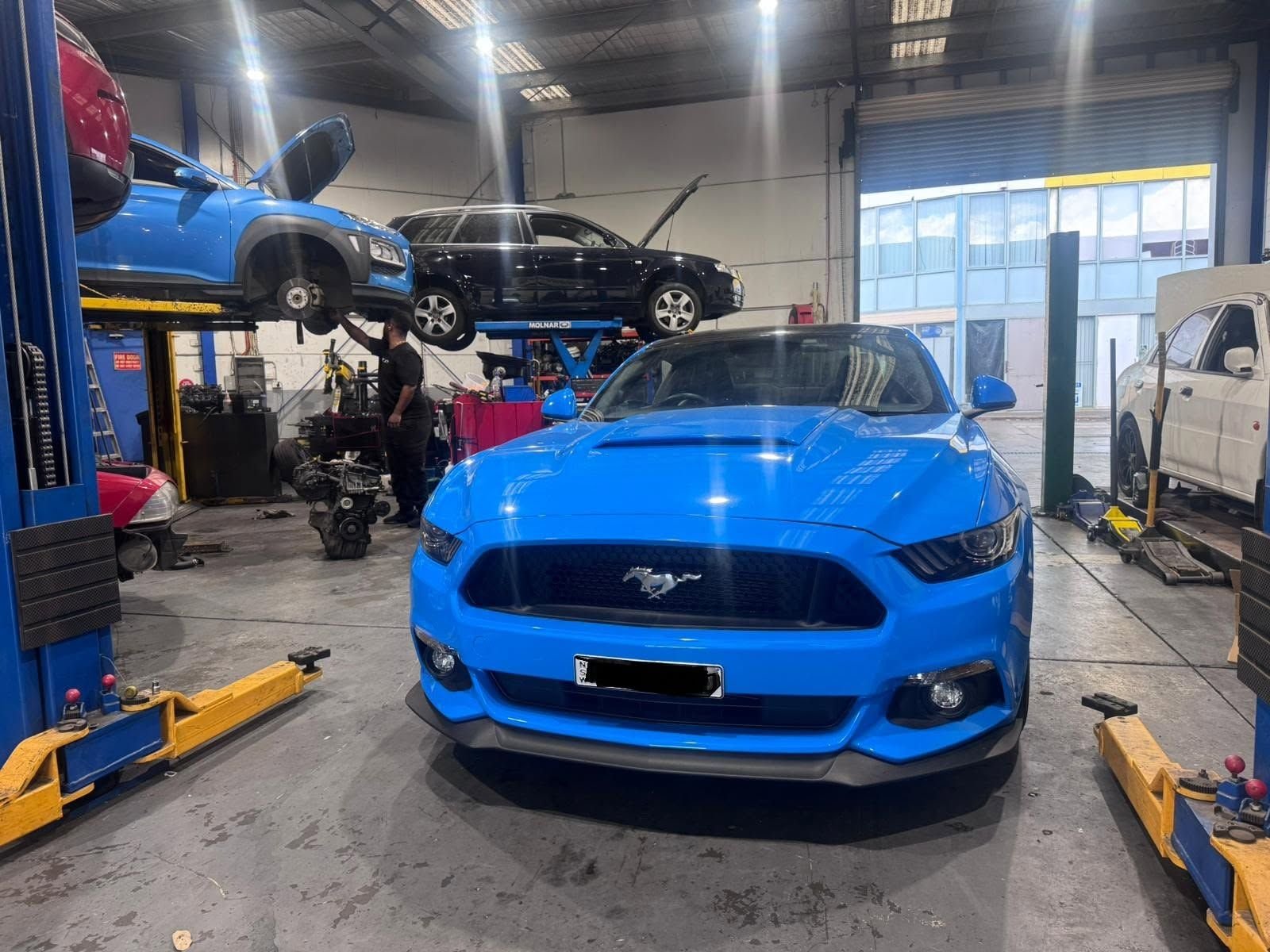 Blue Ford Mustang GT parked in the workshop between two hoists
